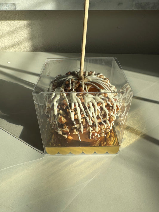 A caramel apple with white drizzle and chopped pecans